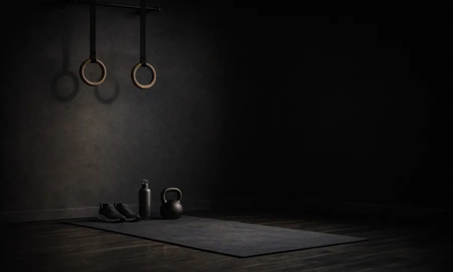 Movement lesson art: a minimalist movement practice corner with mat, rings, shoes, water bottle, and kettlebell in a calm dark room